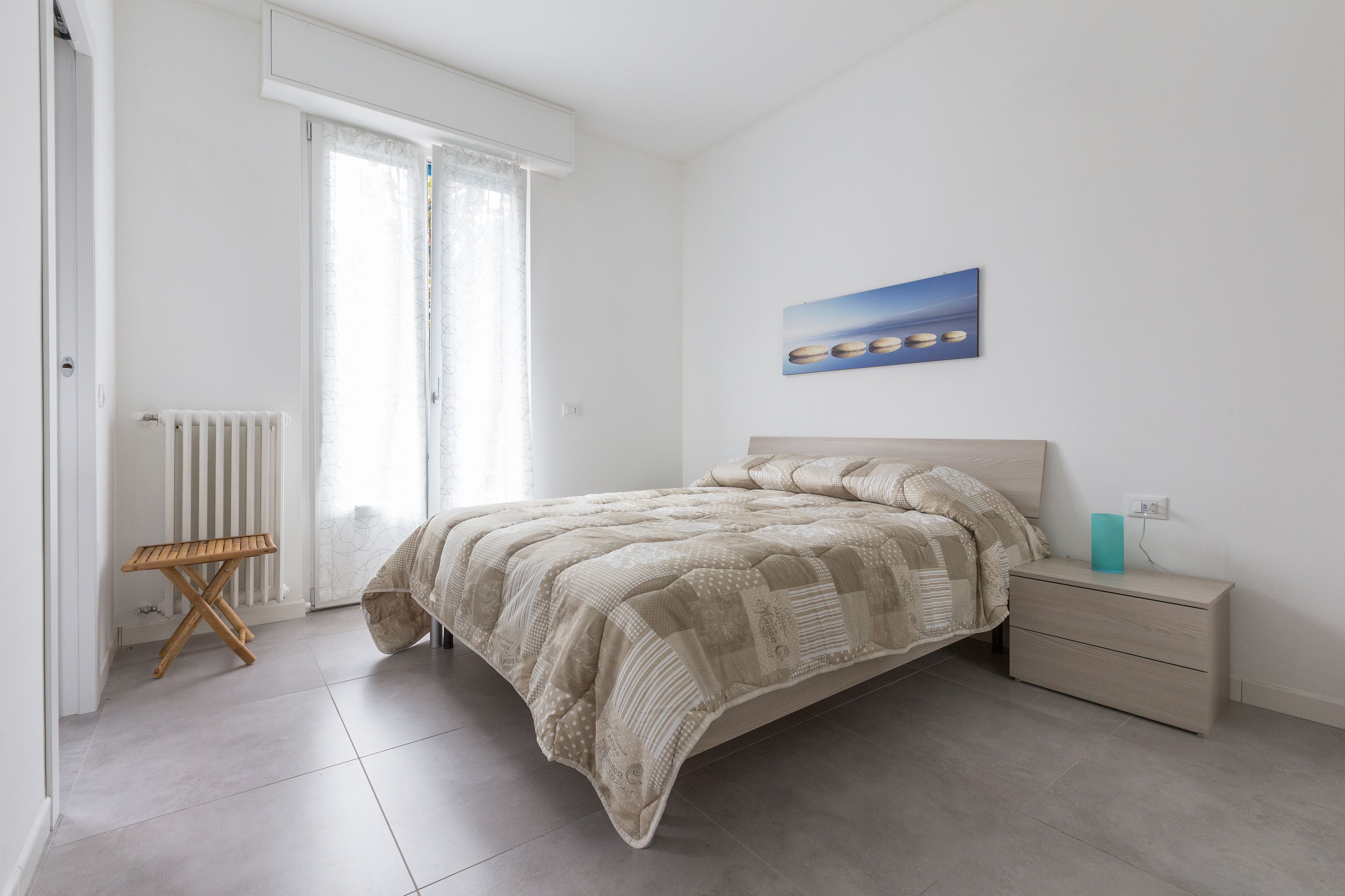 A bedroom with a bed, a bedside table, a radiator, and a window with curtains.