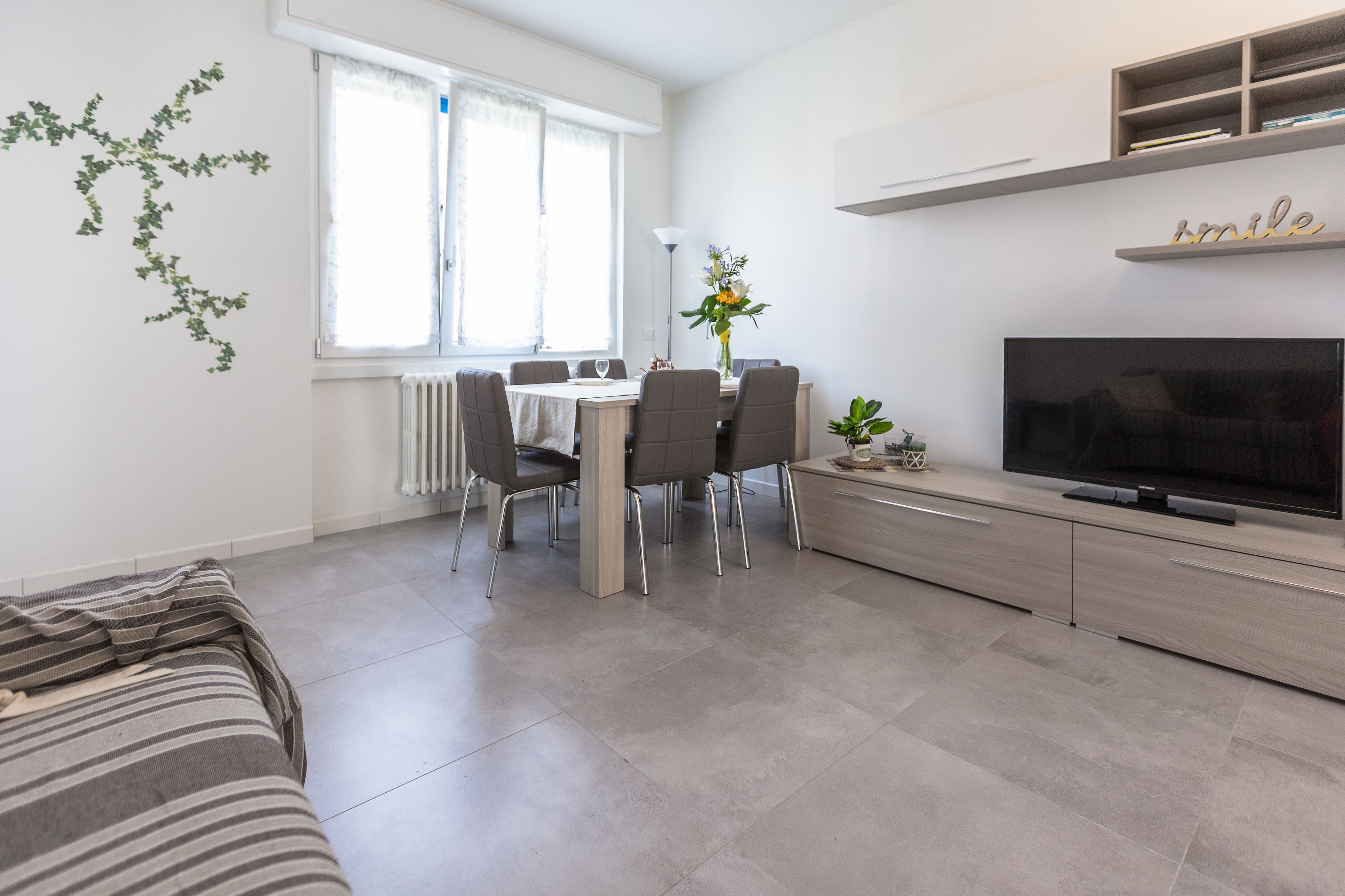 Ein modernes Wohnzimmer mit einer Couch, einem Esstisch mit Stühlen, einem Fernseher und einem Bücherregal.