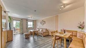 Uma sala de estar ampla com sofá, mesa de jantar com cadeiras, armário de madeira e varanda com vista.