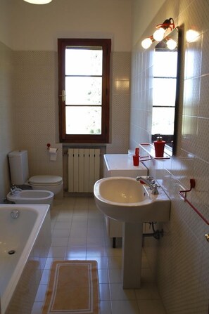 Un baño con bañera, inodoro, bidé, lavamanos y una ventana con vistas.