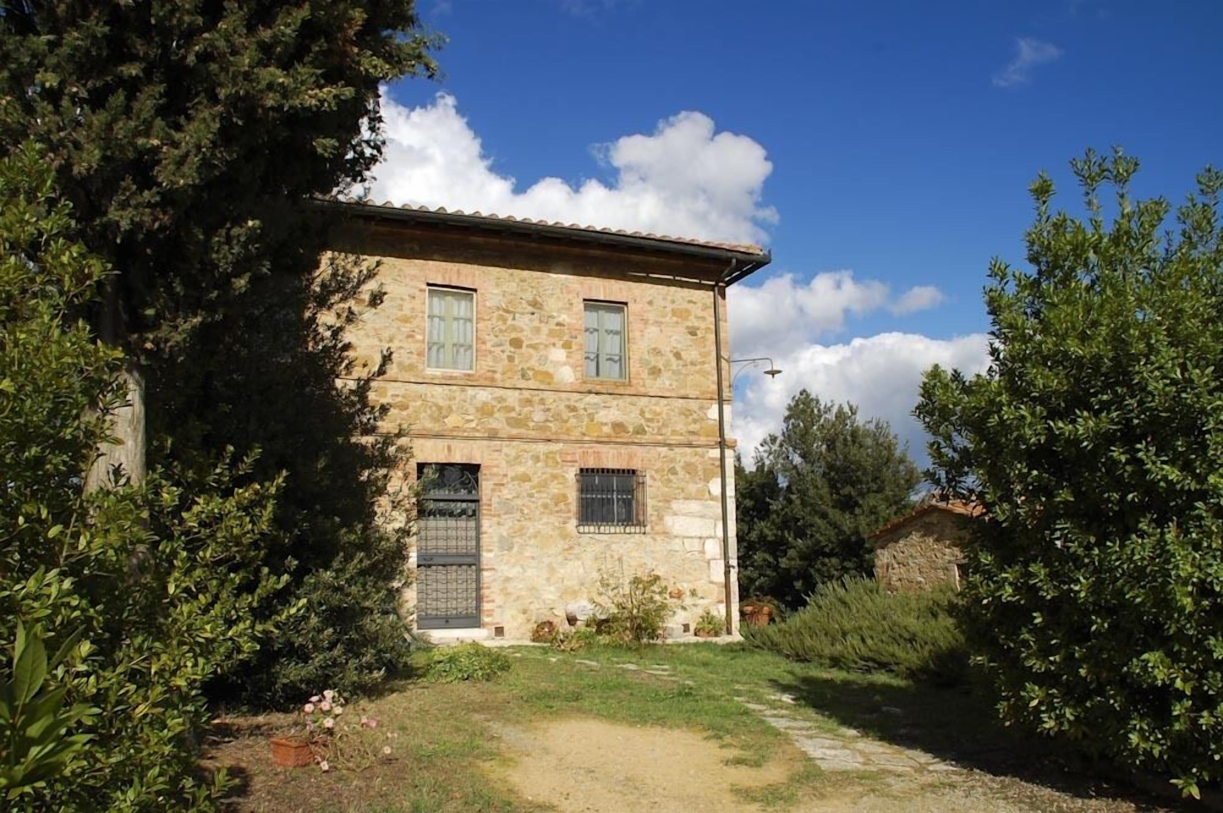 A two-story stone building with a rustic appearance, surrounded by greenery and a clear sky.