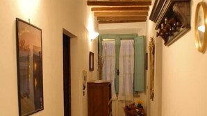 Un couloir étroit avec un sol carrelé, des poutres en bois au plafond, une porte sur la gauche et une fenêtre avec des rideaux au centre.