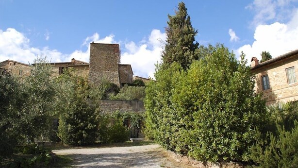 Un bâtiment en pierre doté d ’une tour, entouré de verdure et bordé d’un chemin de gravier.
