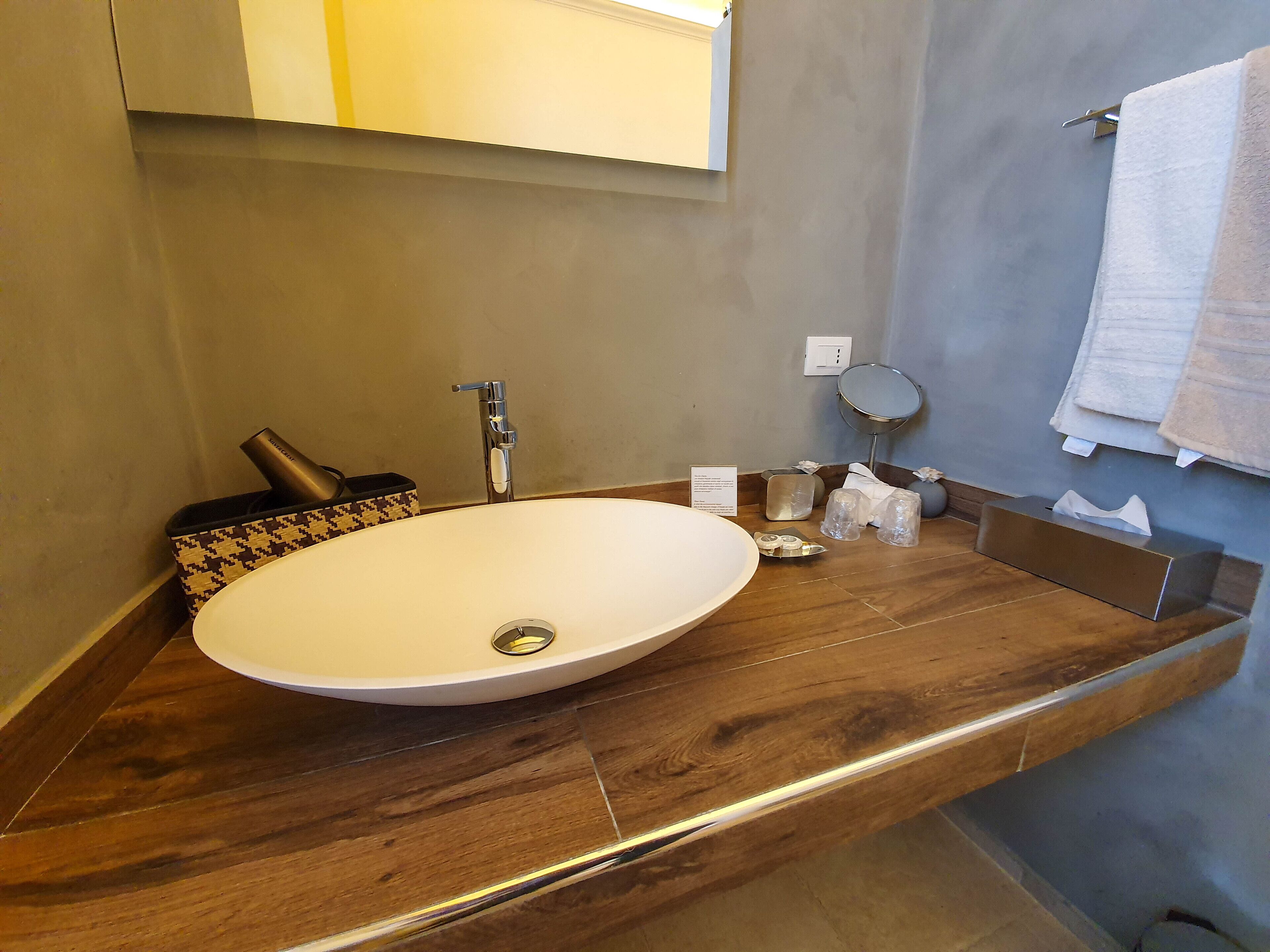 A modern bathroom with a large oval sink, a handheld showerhead, a towel rack, and a mirror.