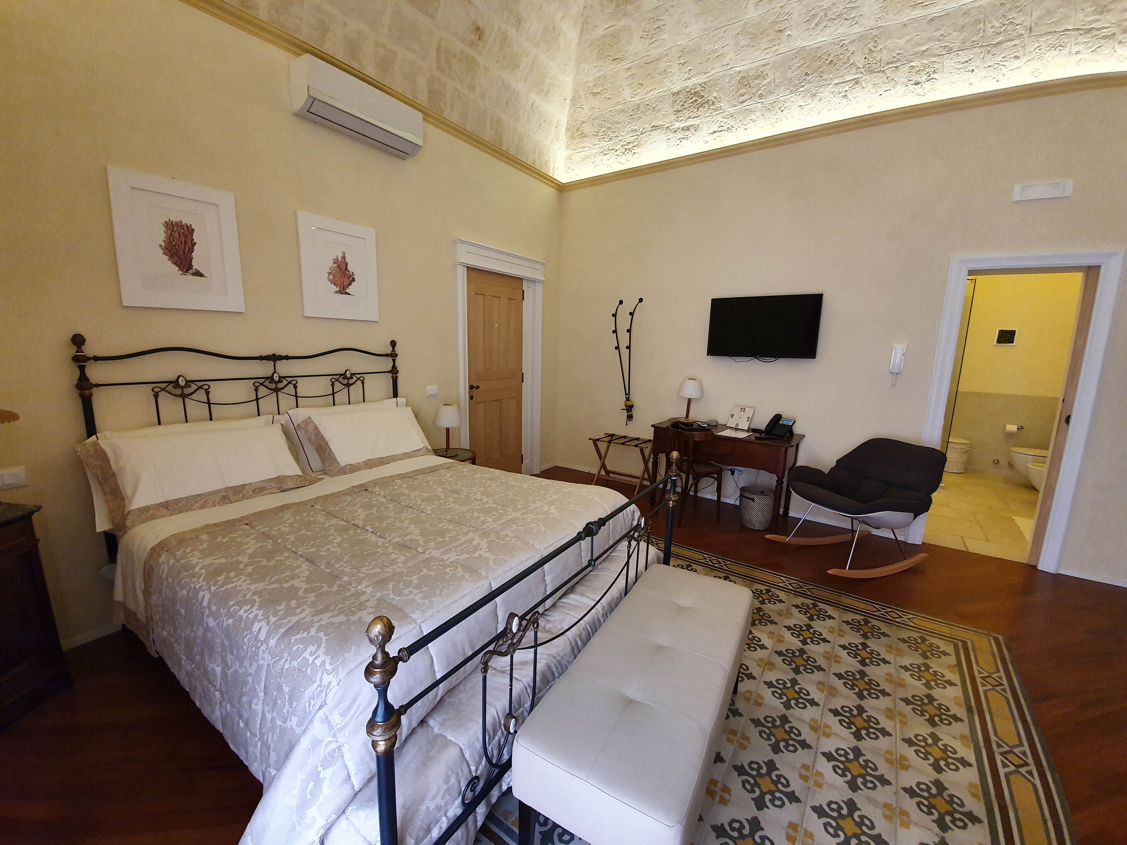 A bedroom with a bed, bedside table, chair, desk, and a television.