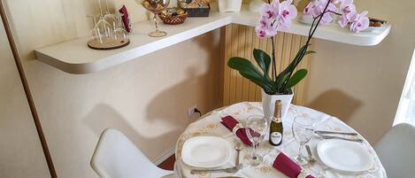 A dining table set with plates, cutlery, and a bottle of wine, with a vase of flowers and a plant on the table.