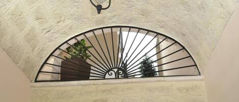 A stone ceiling with a single hanging light fixture and a metal-framed window with a decorative design.