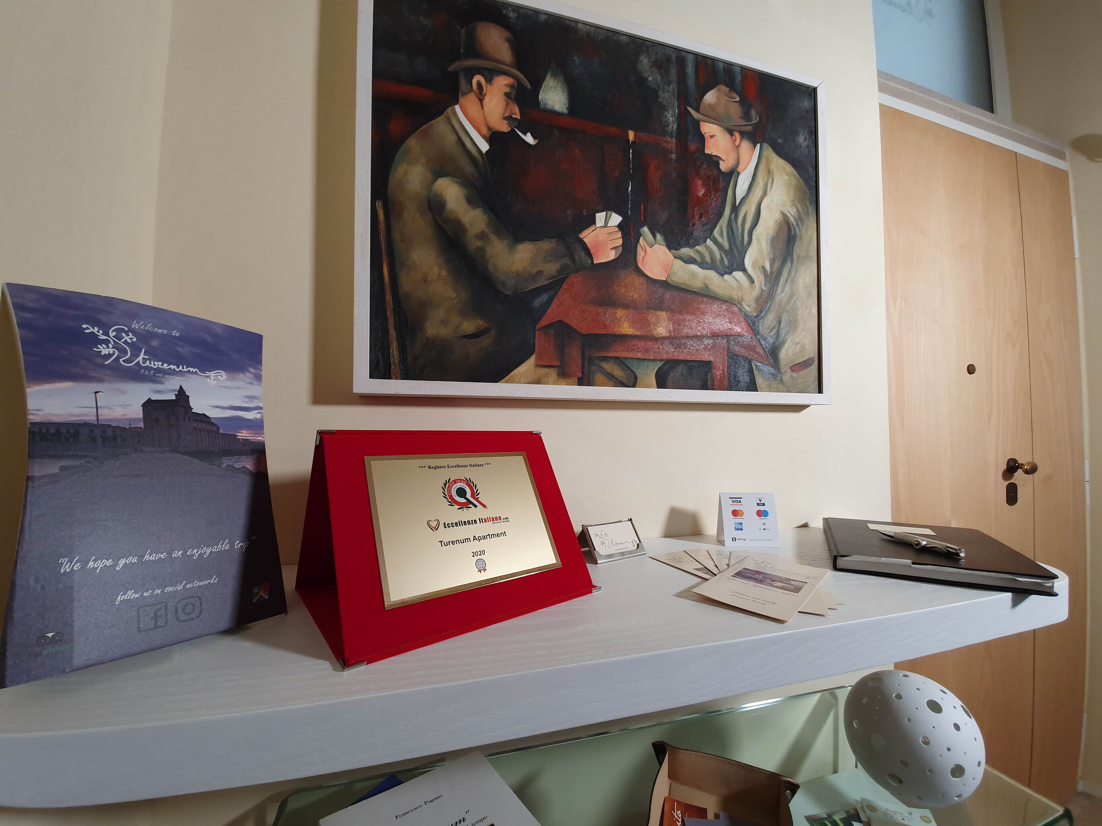 A framed certificate on a desk, a painting of two men playing cards, and a welcome sign for Stremusum.