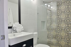 A bathroom with a white sink, a black cabinet, a white toilet, and a shower with patterned tiles. - Nuove Design Lofts by The Spot (Playa del Carmen)
