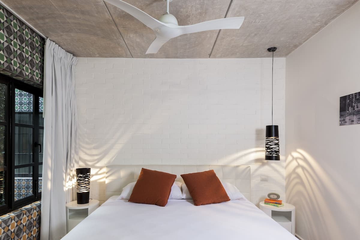 A modern bedroom with a white brick wall, a ceiling fan, and a bed with brown pillows.