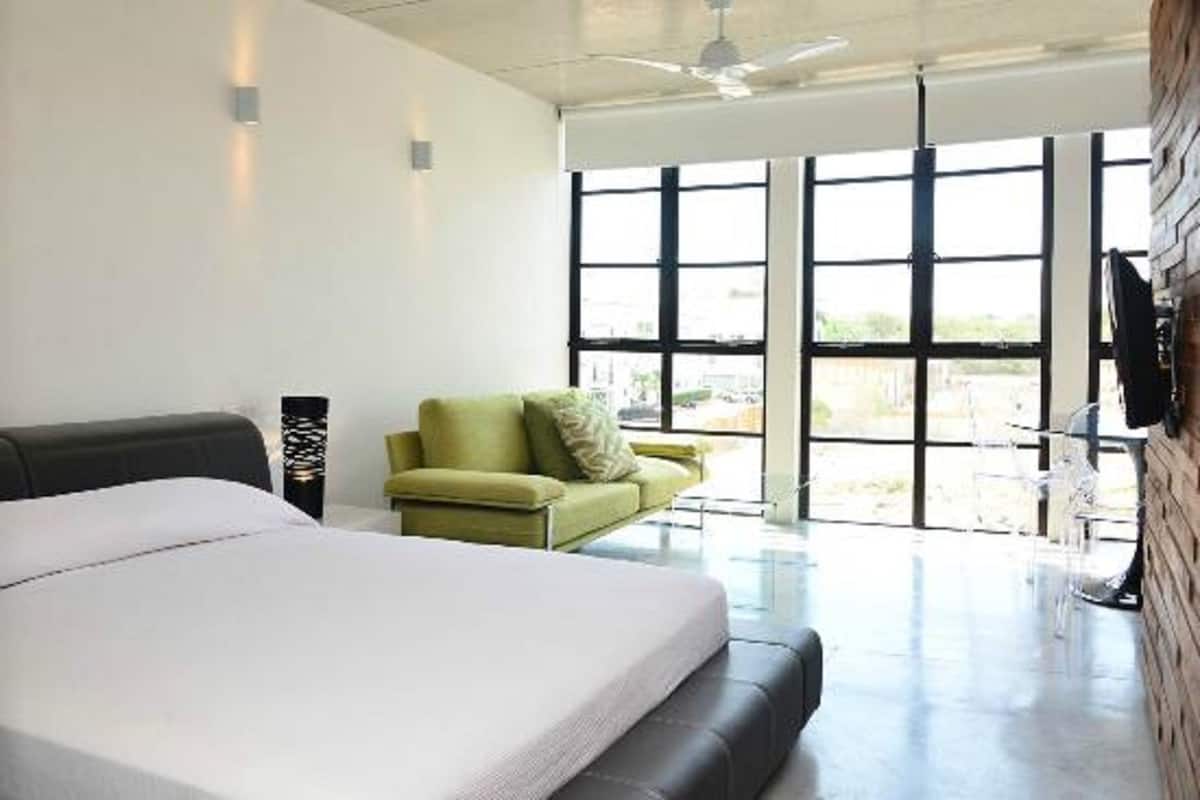 A modern hotel room with a large bed, a green sofa, and a view through large windows.