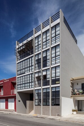 A modern multi-story building with a flat facade, large windows, and a balcony on the upper floor. - Nuove Design Lofts by The Spot (Playa del Carmen)