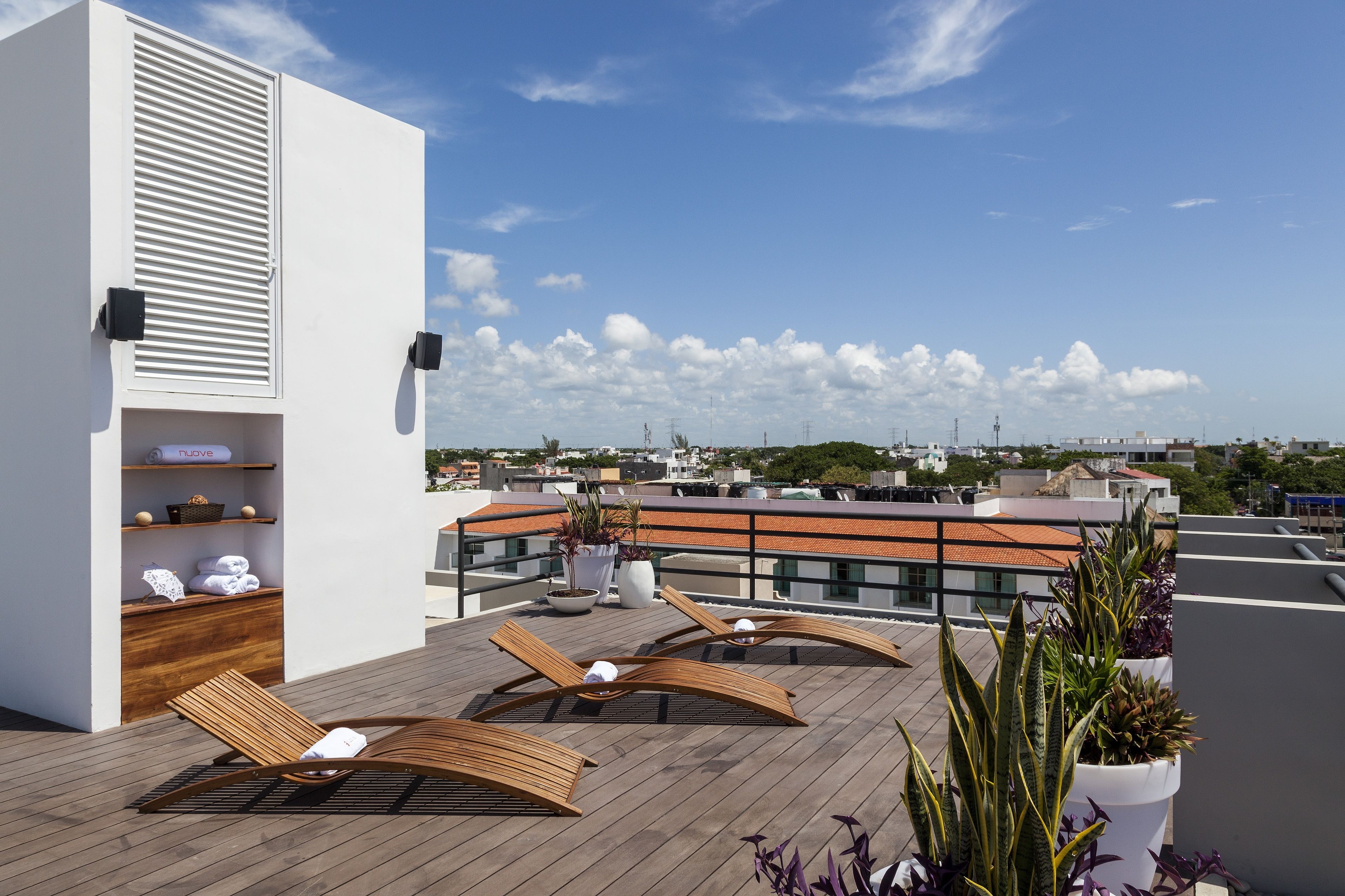 Une terrasse sur le toit avec des fauteuils en bois, un mur blanc doté d’une étagère intégrée et des plantes en pot.