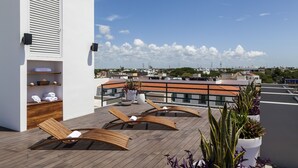 Une terrasse sur le toit avec des fauteuils en bois, un mur blanc doté d’une étagère intégrée et des plantes en pot.