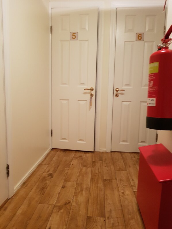A hallway with two white doors, numbered 5 and 6, wooden flooring, and a red fire extinguisher on the right.