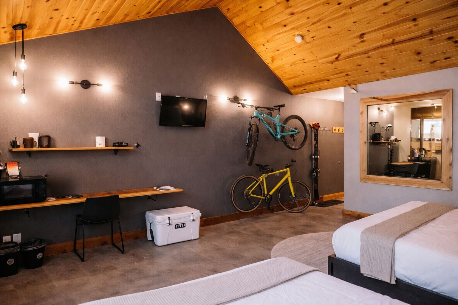 A room with a bed, a desk with a computer, a TV, and bicycles.