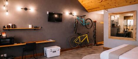 A room with a bed, a desk with a computer, a TV, and bicycles.