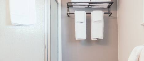 A bathroom with a toilet, a trash bin, a shower, and a towel rack with towels.