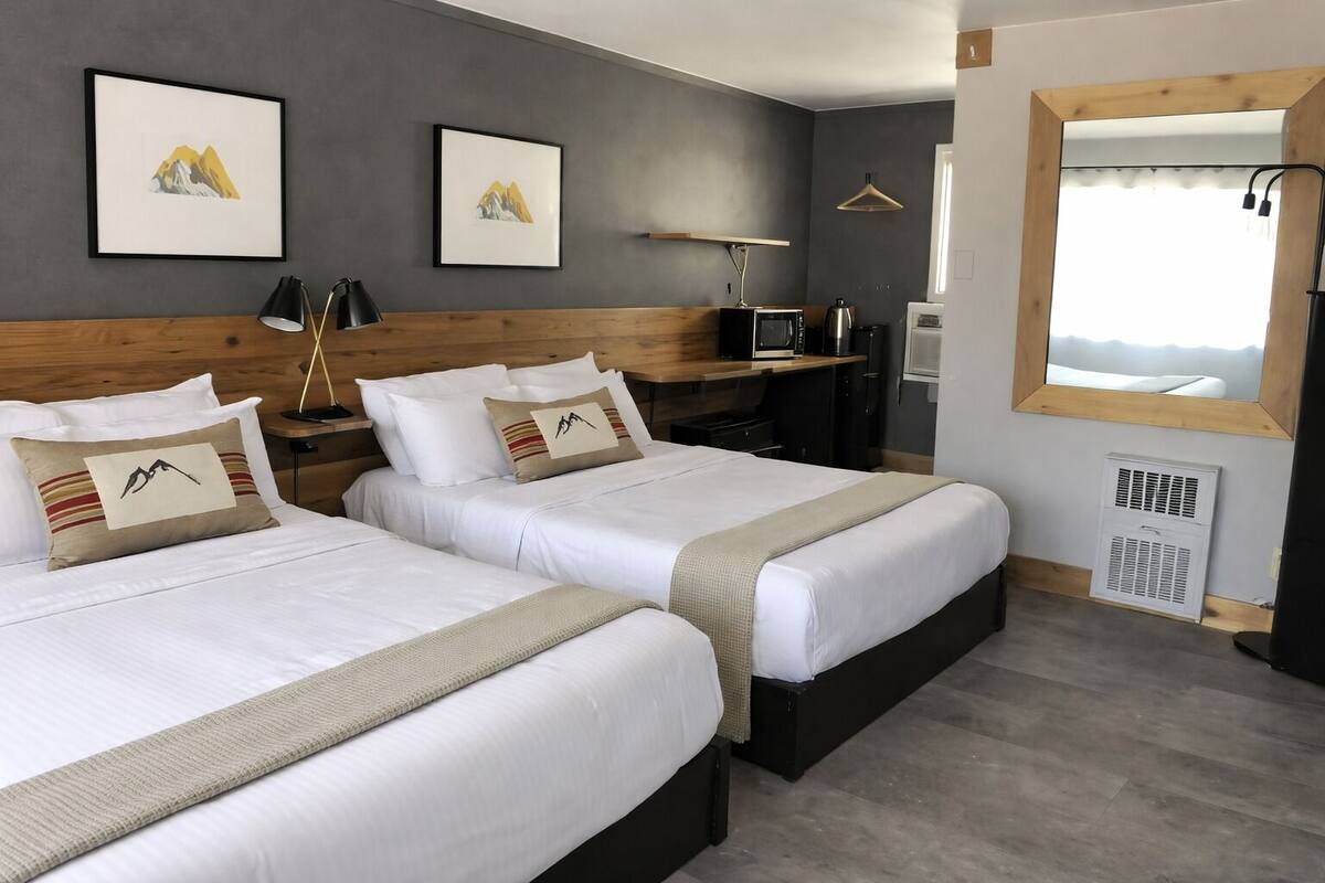 A hotel room with two beds, a wooden headboard, a desk with a computer, a mirror, and artwork on the wall.