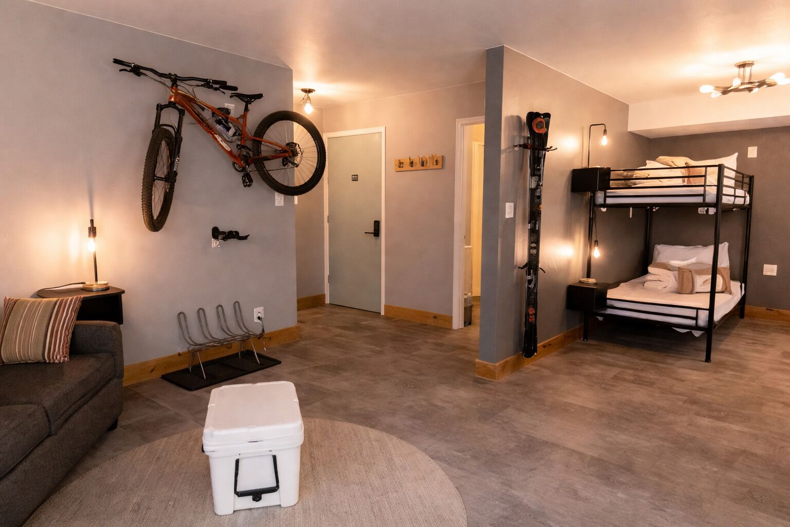 A compact room with a bunk bed, a bicycle mounted on the wall, a couch, a small table, and a storage box.