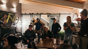 A group of people in a modern indoor setting with bicycles mounted on the wall, a wooden ceiling, and a staircase in the background. - Summit View Inn (Mount Shasta)