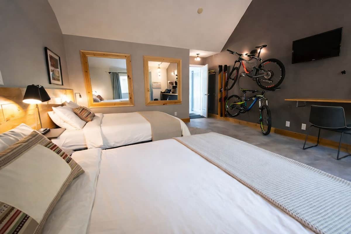 A hotel room with two beds, a desk, a chair, a TV, and bicycles mounted on the wall.