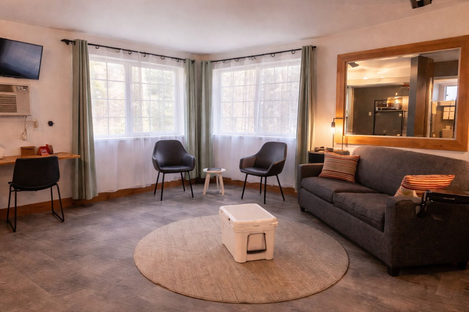 A living room with a sofa, two chairs, a small table, a TV, and a mirror.