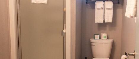 A bathroom with a glass-enclosed shower, a toilet, and a towel rack with multiple towels.