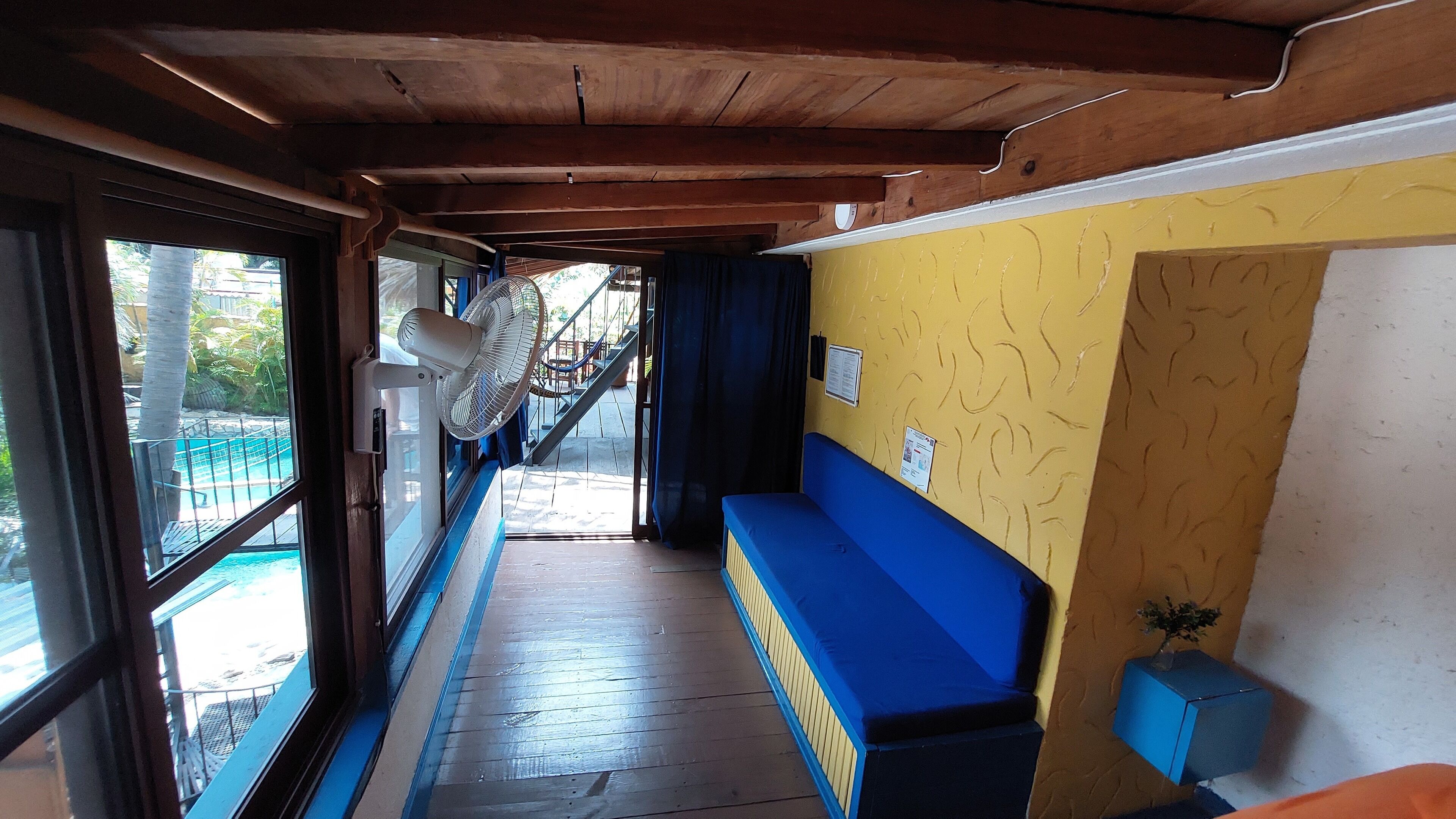 Un couloir avec un plafond en bois, un banc bleu et un ventilateur.