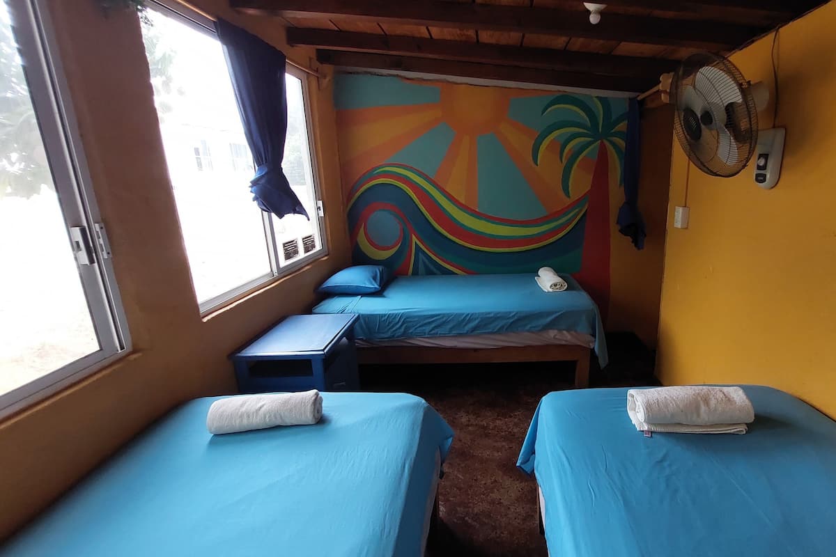 A room with two beds, a window, a wall mural, and a fan.