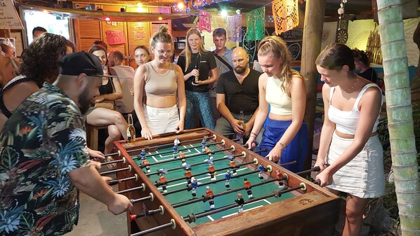 A group of people playing foosball in a room with wooden walls and a dartboard.