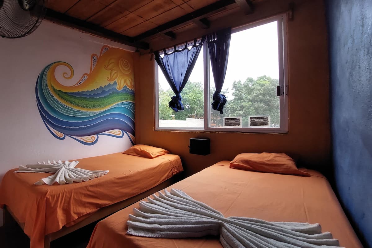 A room with two beds, a mural, a window with curtains, and a fan.