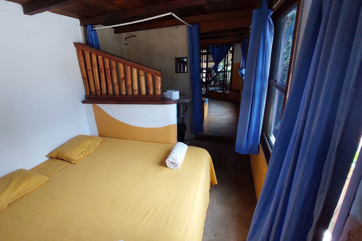 A room with a bed, a wooden staircase, and a window with curtains.