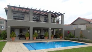 Ein modernes, zweistöckiges Haus mit Swimmingpool, Sitzgelegenheiten im Freien und einer überdachten Terrasse.