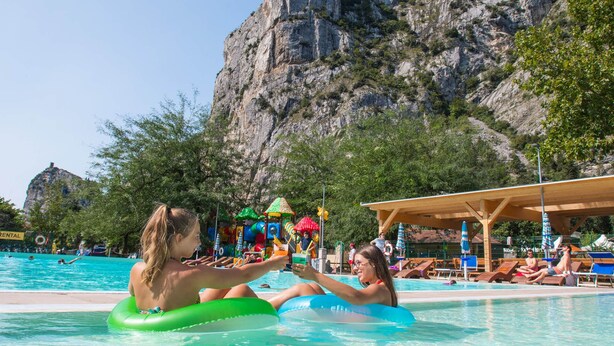 A pool area with inflatable rings, lounge chairs, and a mountainous backdrop.