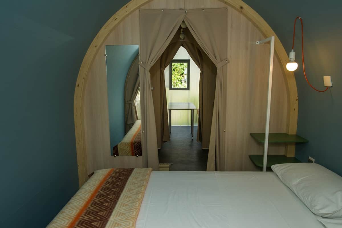 Ein Schlafzimmer mit einem Bett, einem Nachttisch, einer Lampe und Blick durch eine Rundbogenöffnung auf einen Balkon.
