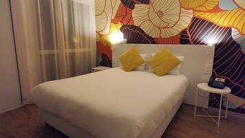 A hotel room with a large bed, a bedside table with a phone, and a colorful floral wall mural.