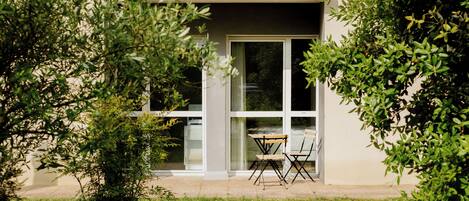 A modern building with a balcony, large windows, and a small outdoor seating area.