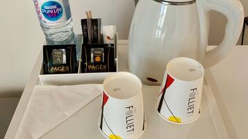 Bandeja con una botella de agua Nestlé Pure Life, dos tazas de café, un juego de té y una tetera eléctrica blanca.