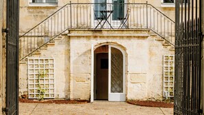 Ein historisches Gebäude mit einem zentralen Bogenportal, einem Balkon mit Metallgeländern und einem Kiesweg, der zum Eingang führt.