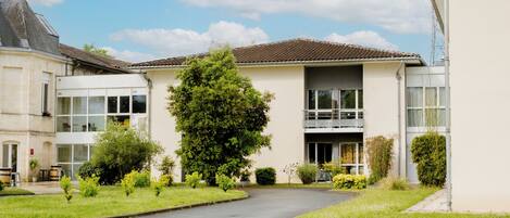 A two-story building with a balcony, surrounded by a well-maintained lawn and a paved driveway.