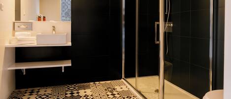 A modern bathroom with a glass-enclosed shower, a white sink, and a patterned floor.