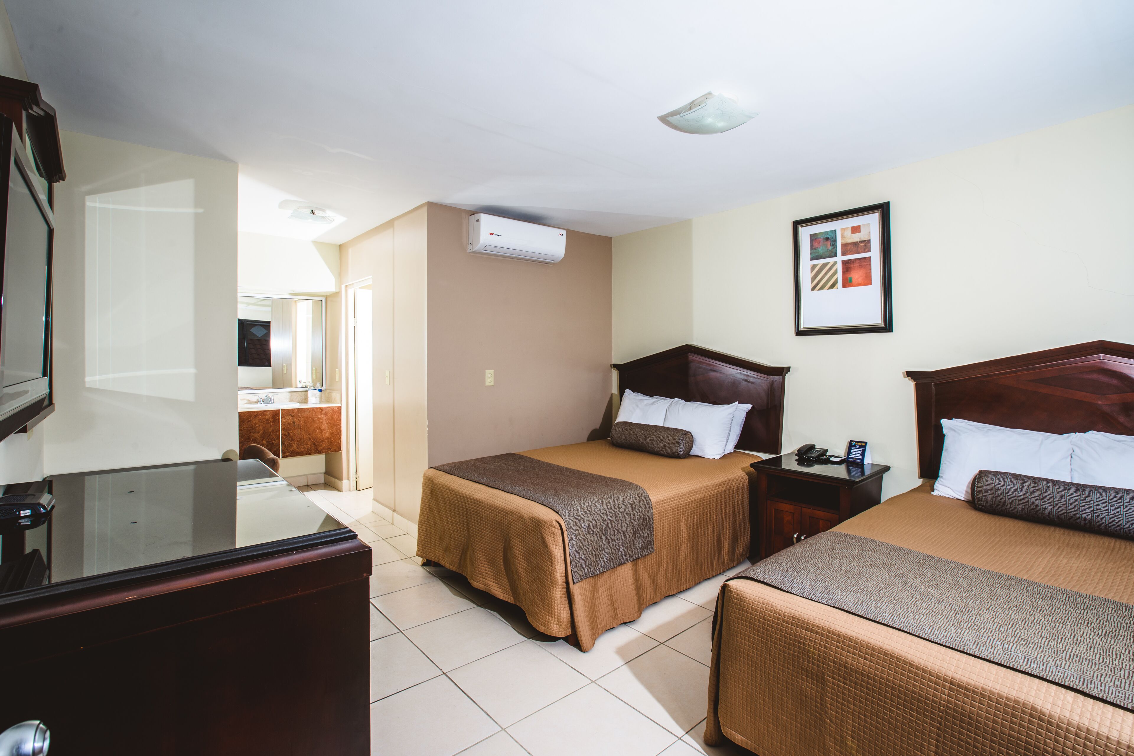 A hotel room with two beds, a desk, a mirror, and an air conditioning unit.