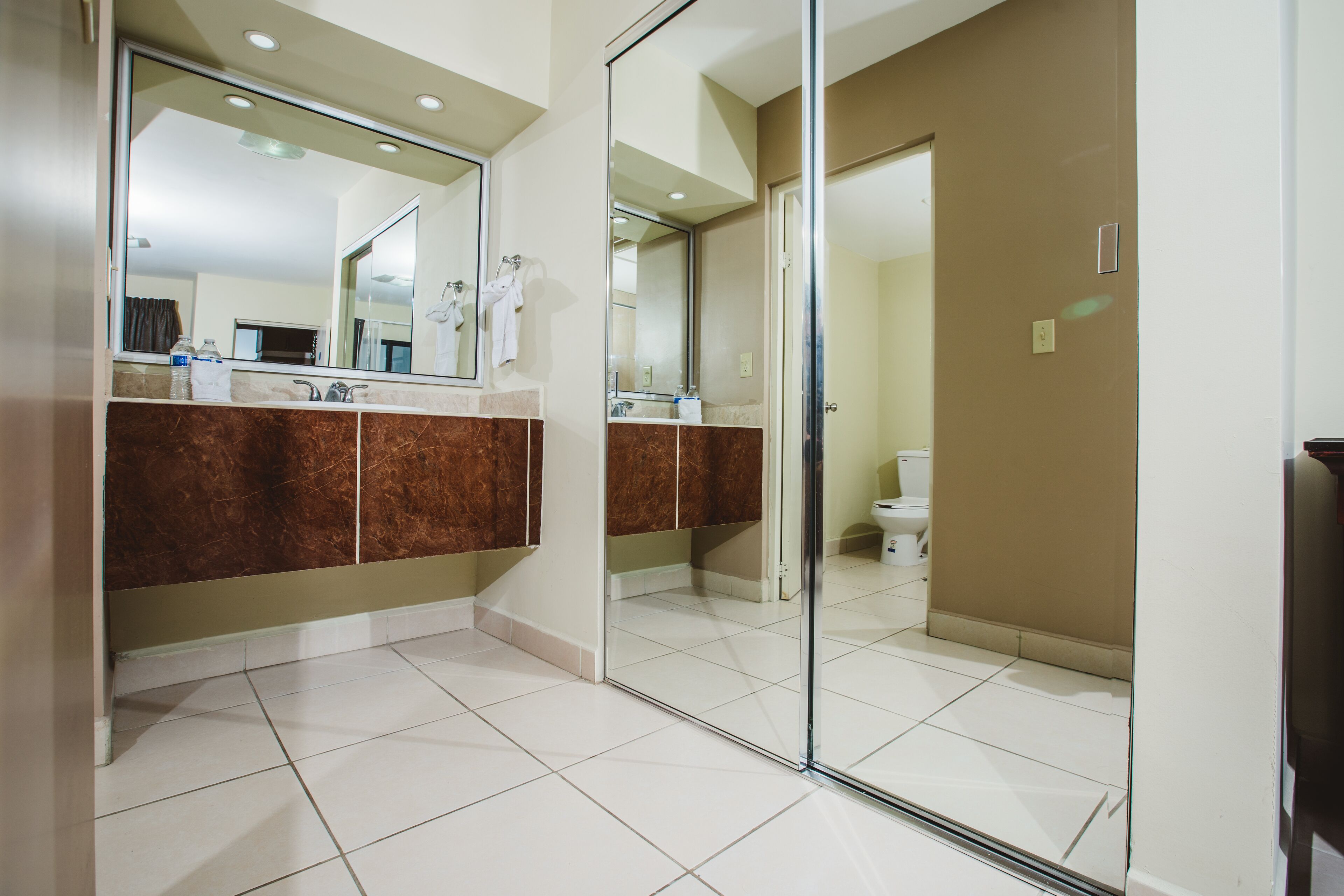 A modern bathroom with a large mirror, a glass shower enclosure, and a toilet visible through the glass doors.