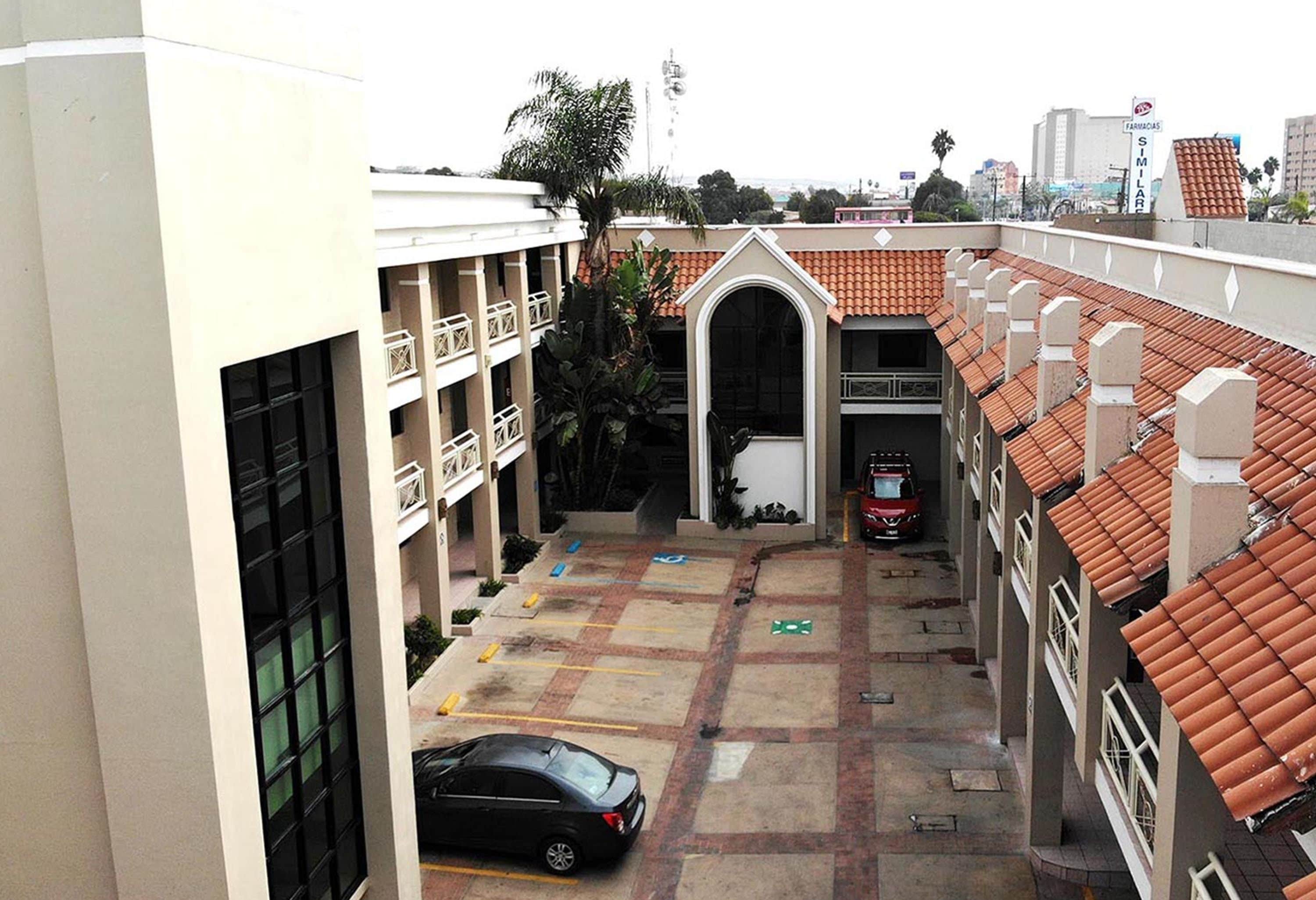 A courtyard with a car parked in the center, surrounded by buildings with red-tiled roofs and balconies.