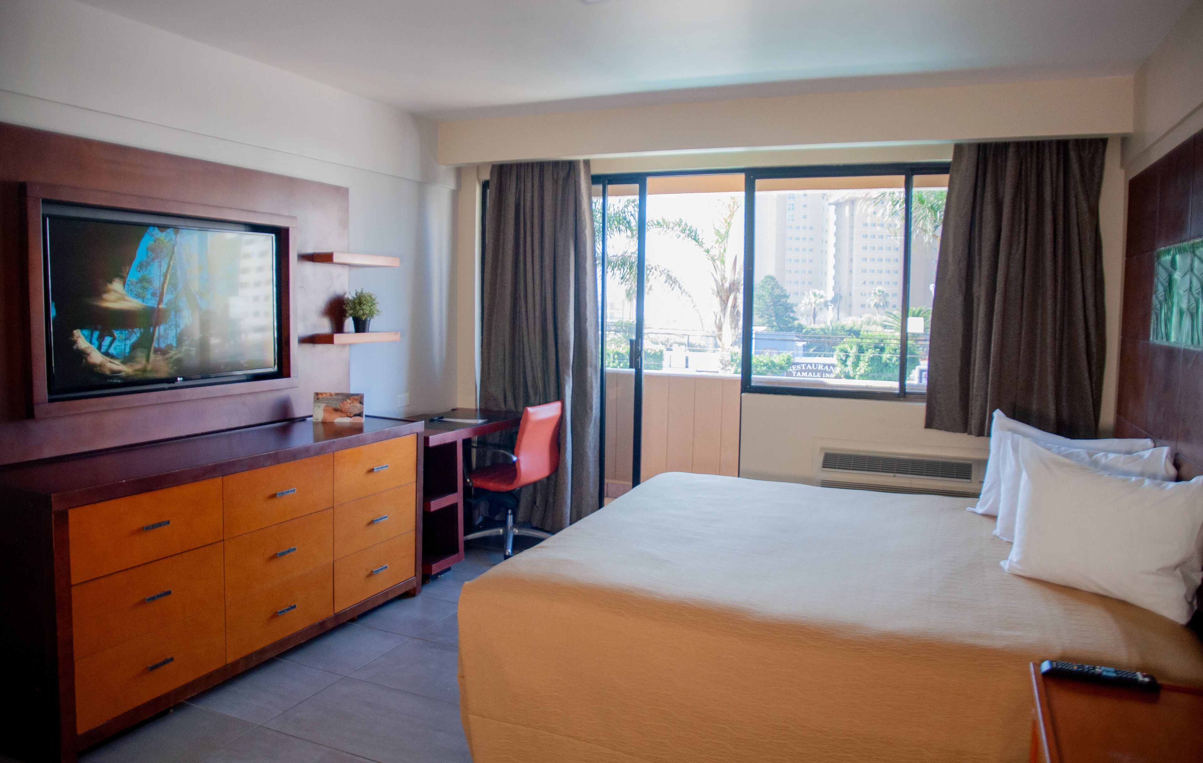 Una habitación de hotel con cama, escritorio, televisión y ventana con cortinas.