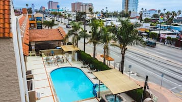A hotel with a swimming pool, outdoor seating, and a view of the cityscape.