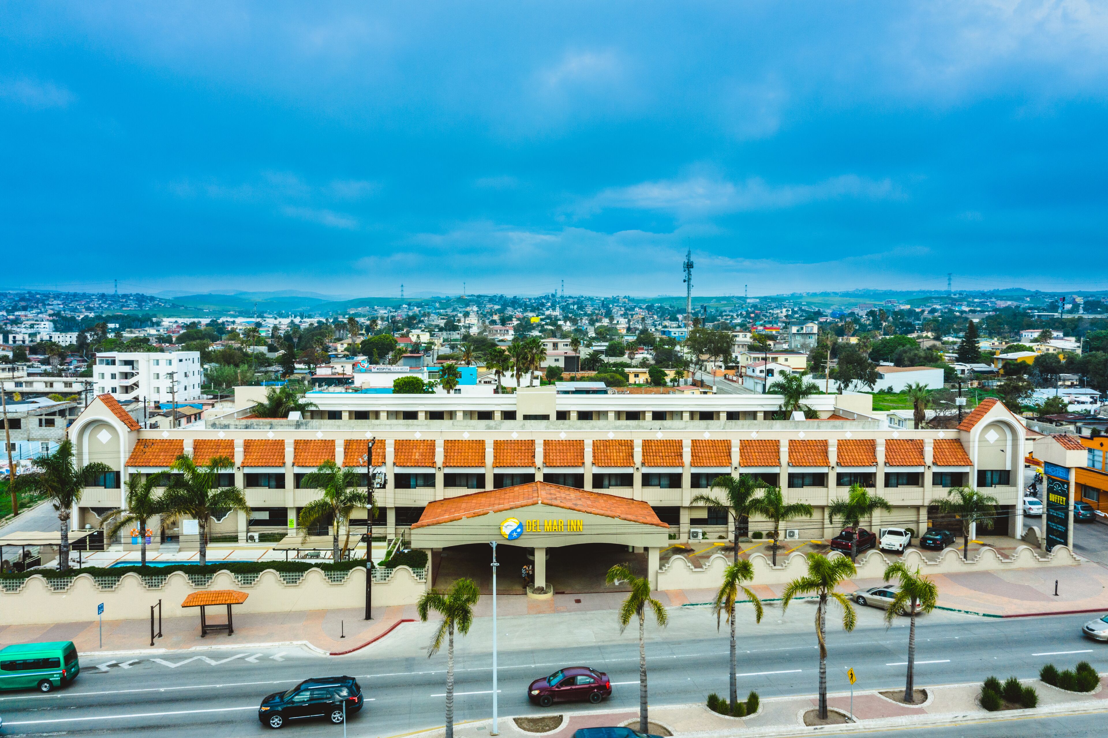 A hotel with a red-tiled roof, a central entrance, and palm trees in front.