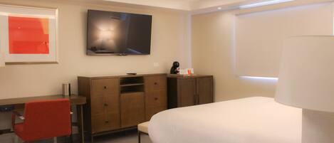 A modern hotel room with a bed, a desk, a chair, a television, and a cabinet.