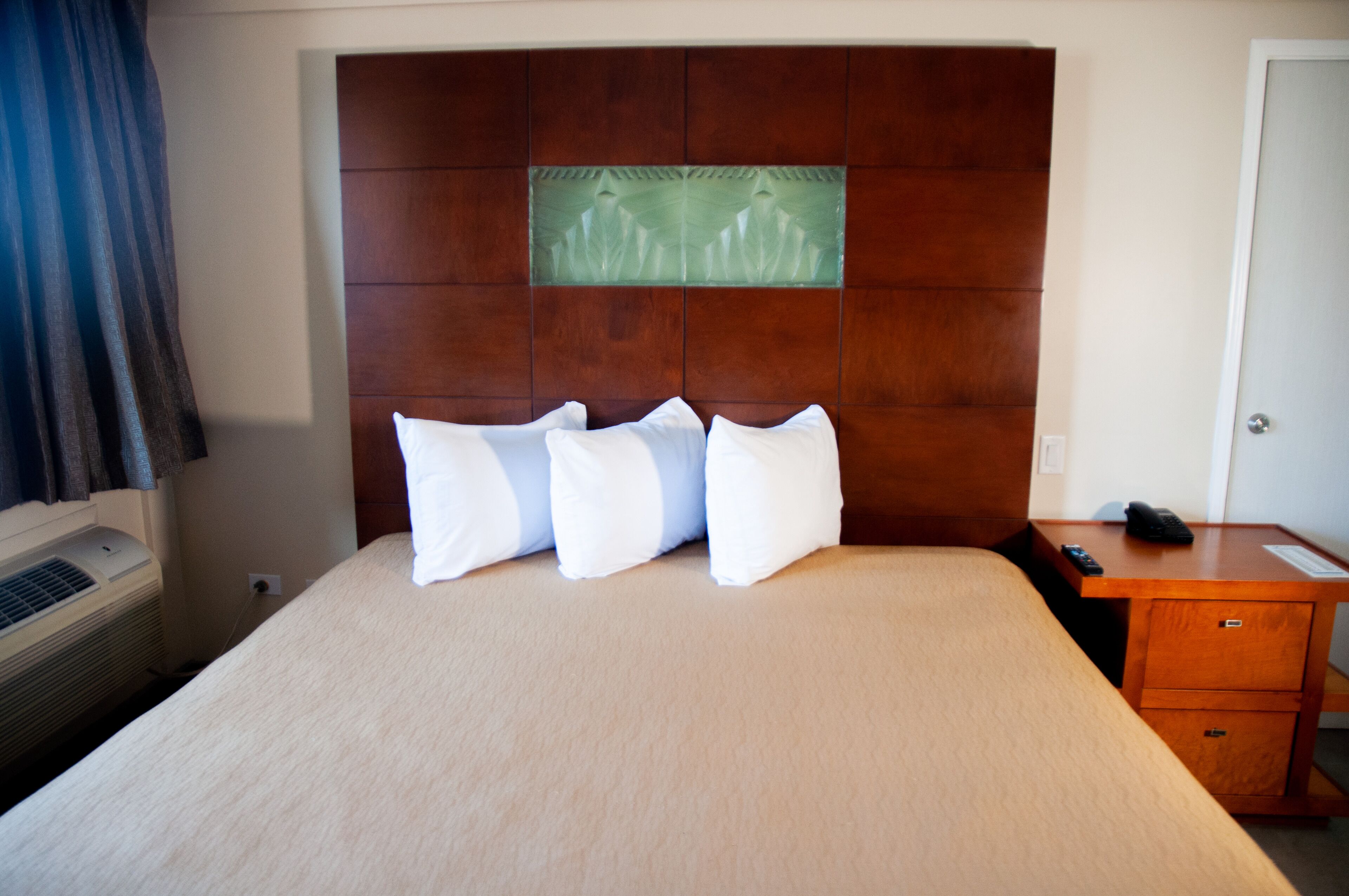 Habitación de hotel con una cama grande, un cabecero de madera, un escritorio pequeño con teléfono y aire acondicionado de pared.
